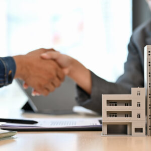 People shaking hands over a table with paperwork and a miniature condo on the table