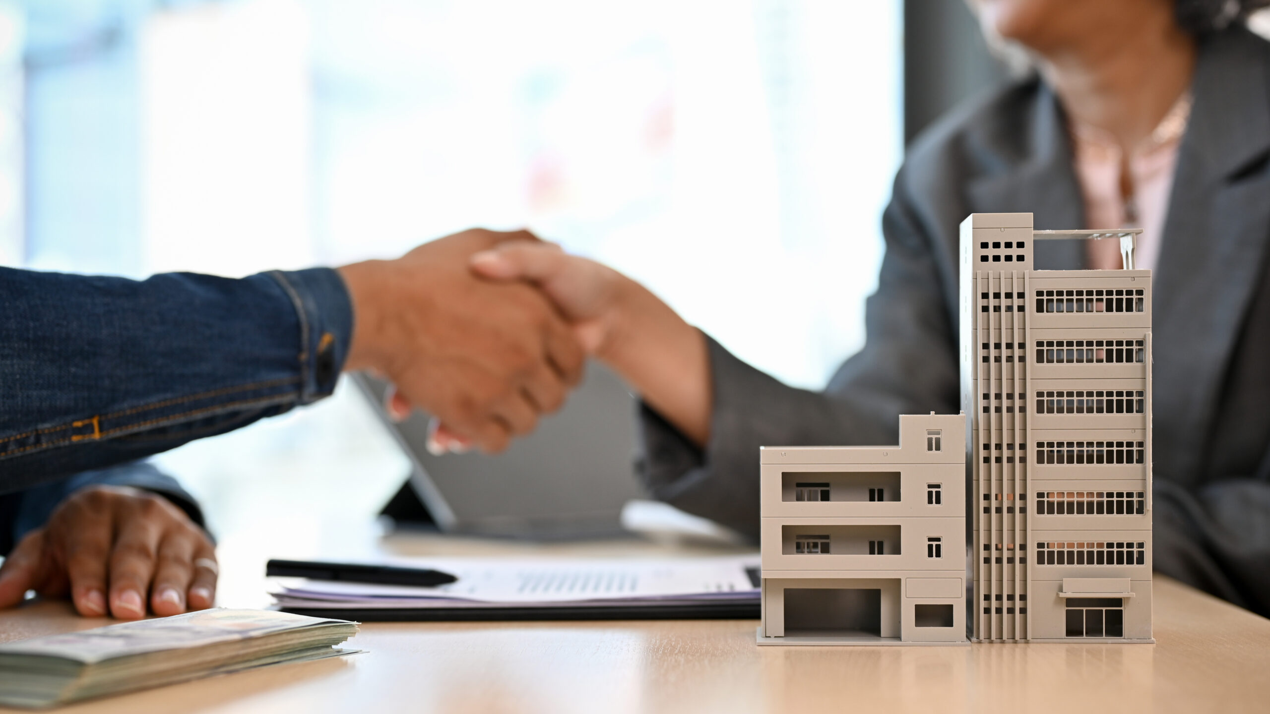 People shaking hands over a table with paperwork and a miniature condo on the table